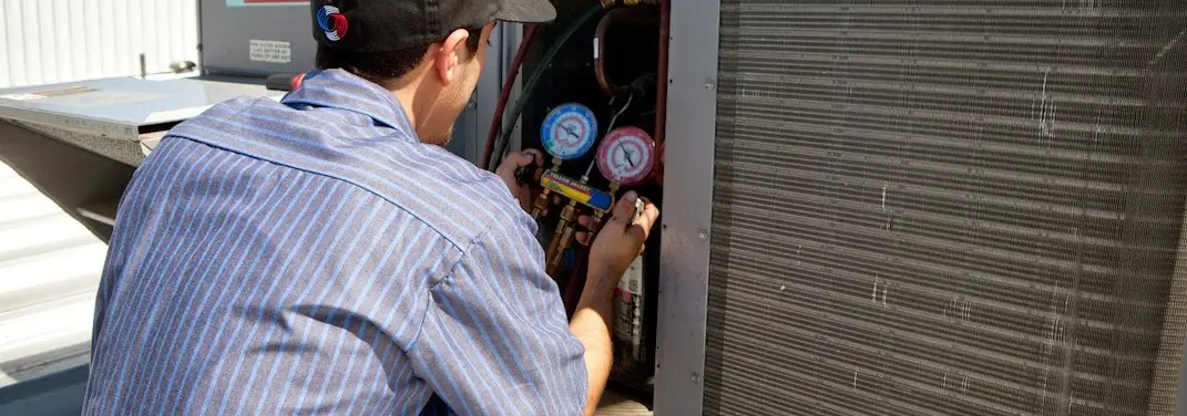 HVAC technician servicing a condenser unit in Elba